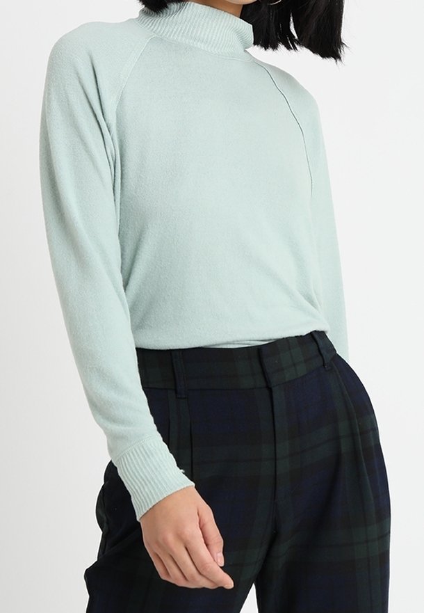 Licht mintgroen turtlenecktrui met een zachte textuur, raglanmouwen en geribbelde manchetten, gecombineerd met donker geruite broeken.