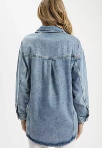 Niebieska, oversize koszula dżinsowa o długich rękawach, z kołnierzem, szczegółem w postaci pliski z tyłu oraz zaokrąglonym dołem. Miękka faktura i swobodny fason.