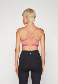 Rozā sporta krūšturis ar krustojošām siksnām un režģa detaļām, ar regulējamiem āķiem un teksturētu joslu. Apvienots ar melnām, augsto vidukli sasniedzošām legingām.
