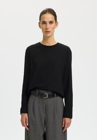 Black long-sleeve shirt made of soft fabric, paired with high-waisted gray trousers featuring a textured pattern and a black belt.