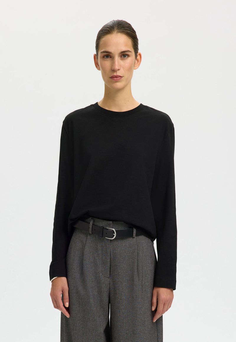 Black long-sleeve shirt made of soft fabric, paired with high-waisted gray trousers featuring a textured pattern and a black belt.