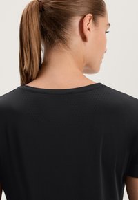 Top atletico nero con scollatura rotonda, dotato di piccole perforazioni sulla schiena per la ventilazione e una texture morbida e liscia.