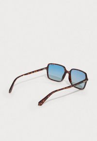 Gafas de sol carey con montura cuadrada y lentes degradados en azul. Cuenta con patillas delgadas con acentos en dorado y acabado pulido.