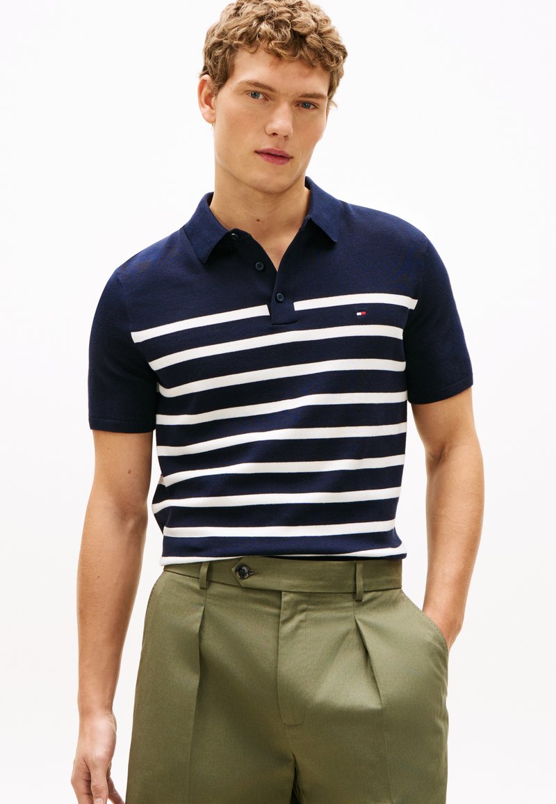 Marineblå og hvide stribede kortærmede polo med krave, der har en lille logo på brystet, parret med lysegrønne skræddersyede bukser.