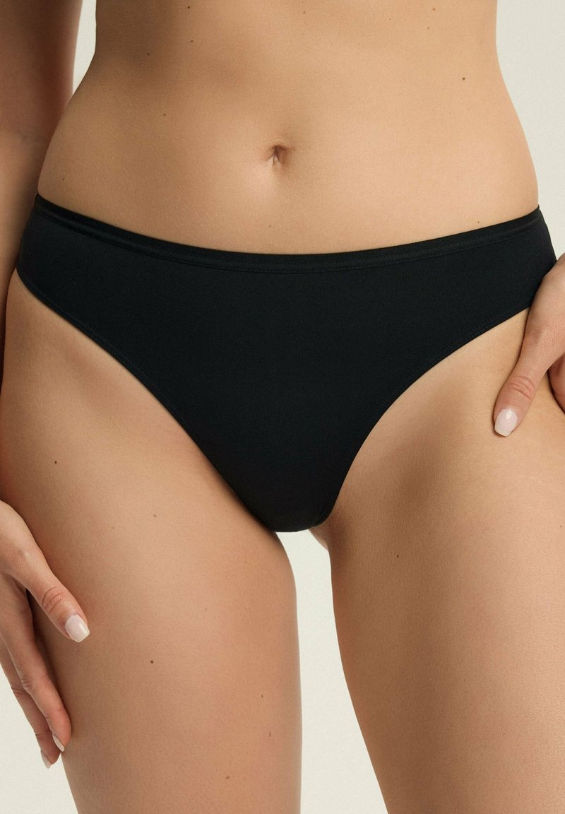 Czarny dół bikini wykonany z gładkiego materiału. Charakteryzuje się wysokim krojem oraz elastycznym paskiem w talii, oferując minimalne zakrycie i bezszwowy wygląd.