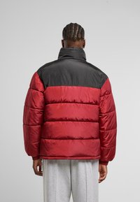 Giacca imbottita rossa e nera con colletto alto, caratterizzata da una texture opaca, design trapuntato e polsini elasticizzati.