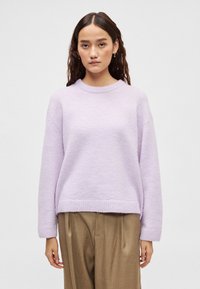 Μπλούζα σε αποχρώσεις λιλά, απαλής υφής, με στρογγυλή λαιμόκοψη, ριμπ μανσέτες και τελείωμα, ελαφρώς φαρδιά εφαρμογή, σε συνδυασμό με μπεζ παντελόνια, ουδέτερο φόντο.