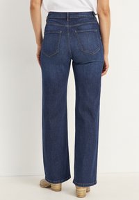 Tummansiniset leveälahkeiset farkut, joissa on kaksi takataskua ja siisti viimeistely lahkeissa. Yhdistetty vaalean värisiin korkokenkiin.