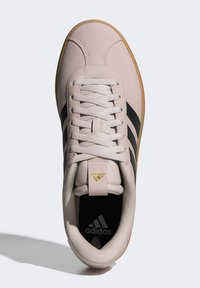 Světle růžové tenisky s černými pruhy, z materiálu podobného semiši, s plochými tkaničkami a strukturovanou gumovou podrážkou. Zlaté akcenty s logem.