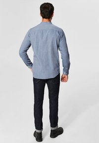 Vaaleansininen chambray-painikkeinen paita, pitkät hihat, suora kauluspanta, yhdistetty tummansinisiin farkkuihin ja mustiin nilkkabootseihin. Yksinkertainen muotoilu, tasaiseen väriin.