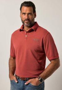 Polo shirt rosso con colletto e maniche corte. Presenta il logo "VINTAGE DENIM" in un colore a contrasto. Indossato con jeans blu e un orologio.