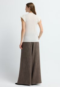 Haut de couleur crème clair avec des mancherons volantés, assorti à un pantalon large en tissu texturé marron. Design simple et minimaliste dans l'ensemble.