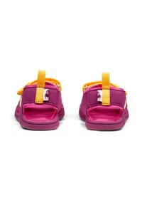 Sandali per bambini viola e gialli con parte posteriore aperta, fasce in tessuto e chiusure in velcro regolabili. Presentano un etichetta con un personaggio colorato.
