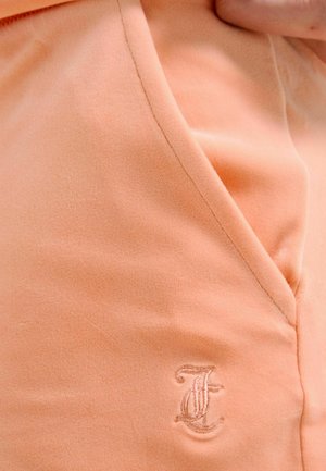 Close-up of peach-colored fabric with stitched seam and embroidered script letter "J" near the edge of a garment.