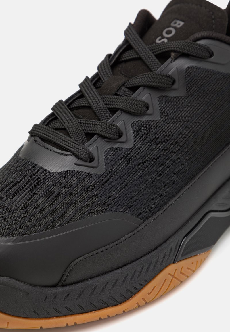 Zwarte sportieve schoen met een bovenwerk van textuurstof, rubberen zool en contrasterende gum buitenzool. Heeft dikke veters en zigzagaccenten aan de zijkanten.