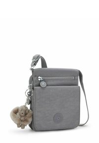 Bolso bandolera de nailon gris con un compartimento con cremallera, bolsillo frontal y un llavero de mono de peluche marrón. Cuenta con una correa ajustable y un logo.