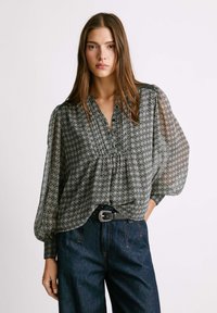 Blusa trasparente a righe bianche e nere con maniche a sbuffo, collo arricciato e orlo elastico, abbinata a jeans scuri a vita alta.
