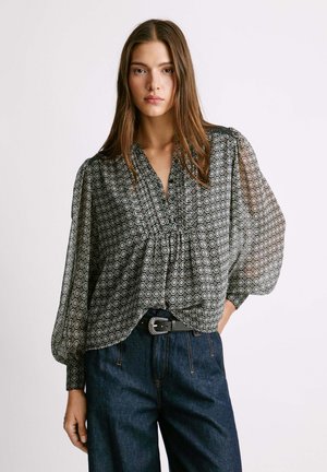 Blusa trasparente a righe bianche e nere con maniche a sbuffo, collo arricciato e orlo elastico, abbinata a jeans scuri a vita alta.