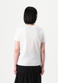 T-shirt branca de algodão com mangas curtas e decote redondo, usada com uma saia preta ajustada. Textura suave, design simples, sem padrões visíveis.