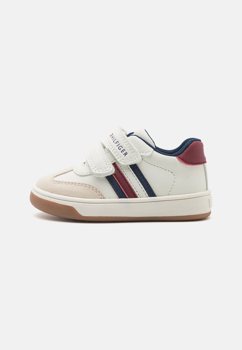 Baskets blanches pour tout-petit avec des rayures bleu marine et rouges, des brides Velcro et une semelle en caoutchouc marron.