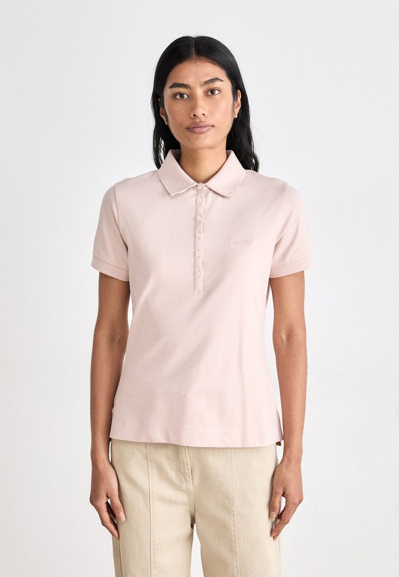 Polo shirt em rosa pálido com colarinho, mangas curtas e fecho de botão frontal. Apresenta um bordado discreto do logótipo no lado esquerdo do peito.
