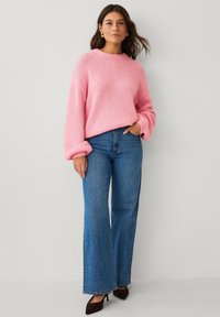 Maglione rosa lavorato a maglia con maniche lunghe e voluminose, abbinato a jeans blu a gamba larga e vita alta e tacchi scuri con punta appuntita.