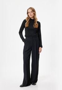 Maglietta nera a maniche lunghe con orlo a costine abbinata a pantaloni neri a vita alta e gamba larga. Tessuto morbido e vestibilità tailored in tutto.