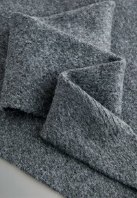 Gråt følt materiale arrangeret i overlappende lag, der viser en blød tekstur og en let ujævn overflade med synlige fibre.