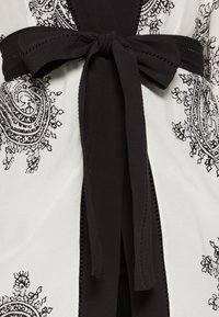 Black and white kimono with paisley pattern, featuring a solid black waist tie and delicate stitching along the edges. Soft fabric texture.