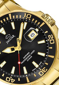 Montre de plongée dorée avec un cadran noir, index horaire luminescents et aiguille des secondes rouge. Elle dispose d'un affichage de la date et d'un verre saphir.