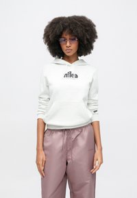 Ανοιχτό γκρι φούτερ με κουκούλα και μπροστινή τσέπη καγκουρό, με μαύρο λογότυπο "Nike", συνδυασμένο με φαρδιά μοβ παντελόνια με ελαστική μέση.