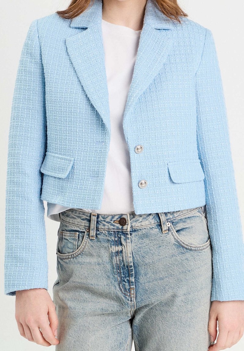 Hellblau, strukturierte, kurze Jacke mit einem strukturierten Design, die einen Reverskragen, zwei Fronttaschen und silberne Knöpfe besitzt.