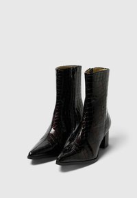 Melnas lakotās ādas potītes zābaki ar krokodila tekstūru, smailu purngali, un blokveida papēdi; ar sānu rāvējslēdzēju, kas atvieglo uzvilkšanu.