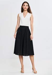 Biała bluzka bez rękawów z dekoltem w kształcie V, w połączeniu z czarną spódnicą w kształcie litery A z plisami, na neutralnym tle.