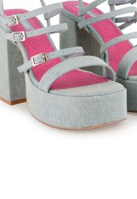 Zapatos de tacón de plataforma de denim con múltiples correas, color azul claro, plantillas rosas y hebillas doradas. Diseñados con un tacón grueso y punta redonda.
