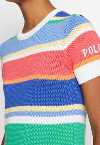 Stickad kortärmad tröja med horisontella ränder i blått, grönt, rött, vitt, gult och orange som bärs av en person.