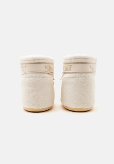 Paire de bottes duveteuses couleur crème avec des semelles de couleur crème clair, vue de dos, montrant une large bride avec le texte "MOON BOOT".