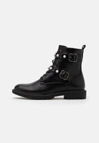 Bottine en cuir noir avec deux sangles à boucle, accents de perles et laçage à l'avant. Semelle texturée remarquable pour une meilleure adhérence.