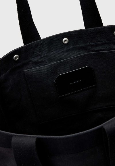 Intérieur d'un sac cabas en tissu noir avec poche cousue, fermetures à pression et deux poignées robustes.