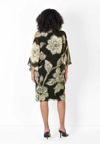 Vestido de chiffon negro con un gran patrón floral beige, mangas sueltas y corte a media longitud, que muestra un diseño fluido y una textura transparente.