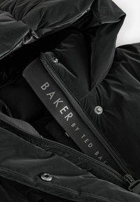 Melna pūču jaka ar rāvējslēdzēju, pogām un teksturētu audumu. Iezīmēta ar uzrakstu "BAKER by TED BAKER."