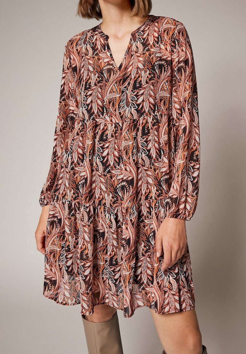 Robe A-line à manches longues en tissu sombre avec des motifs floraux vibrants en orange, blanc et noir. Encolure en V et détail de taille froncée.