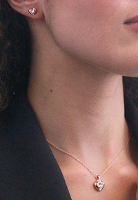 Orecchini a forma di cuore in oro rosa e collana coordinata con una pietra preziosa trasparente al centro, caratterizzati da una delicata catena e una superficie liscia.
