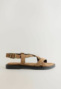 Sandale en daim marron avec brides croisées, boucle ajustable à la cheville, semelle plate noire, semelle intérieure texturée et design ouvert à l'avant.