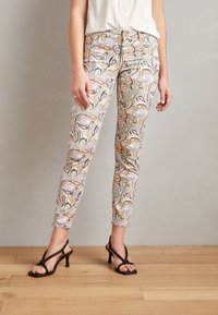 Páskové, slim-fit kalhoty v pastelových barvách s paisley vzorem, vybavené zipem a kapsami, doplněné o černé sandály na podpatku.