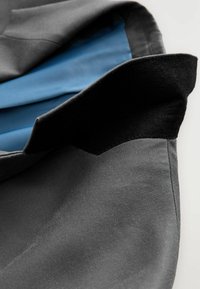 Grauer Stoff mit glatter Textur, blauer Futterung und einem schwarzen Filz-Akzent am Rand, der ein geschichtetes Erscheinungsbild erzeugt.