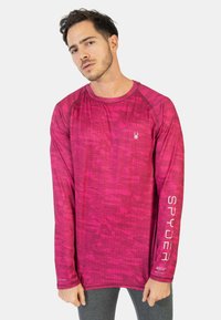 Pitkähihaisen urheilupaidan väri on kirkas pinkki, ja siinä on tekstuuripinnoite. Paidassa on logo rinnassa ja "SPYDER" painettuna hihaan.