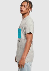 Graues Baumwoll-T-Shirt mit kurzen Ärmeln, das ein blaues Grafikdesign und Text auf der Vorderseite zeigt. Lockere Passform und weicher Stoff.