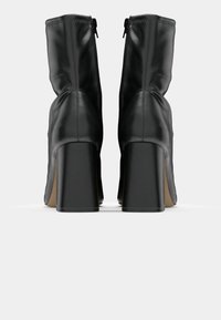 Black leather ankle boots with a high block heel, featuring a sleek design and visible seam details. Zippered closure at the back.