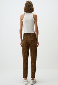 Pantalons taille haute imprimés léopard marron en tissu texturé, avec poches arrière et une coupe fuselée. Associés à un débardeur blanc.